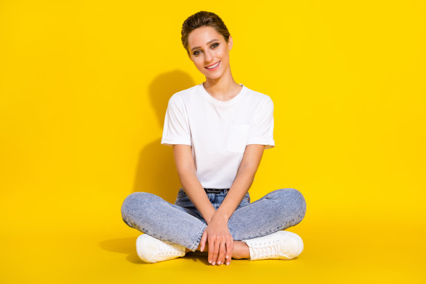 一位留着漂亮棕色发型的千禧年女性，身穿白色T恤和牛仔裤，单独站在黄色背景前，摄于全尺寸照片图片下载