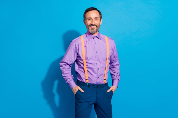 照片：一位成熟的商务男士，带着自信、快乐、积极的微笑，双手插在口袋里，背景为蓝色。图片下载