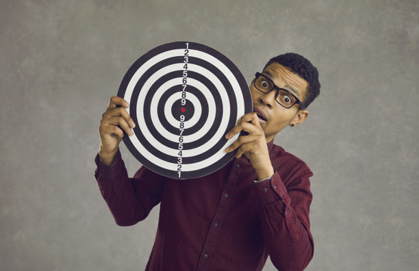 年轻的非裔美国男子，惊恐地站在灰色工作室墙壁前，背景是飞镖盘图片下载