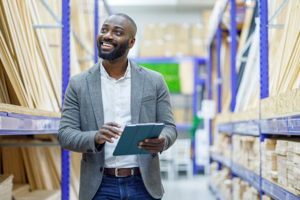 一位黑人男性在微笑，同时使用平板电脑查看股票并管理物流，优化分销和仓储。图片下载