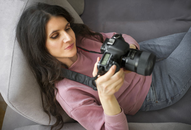 一位女性摄影师坐在沙发上，在相机上查看照片图片下载