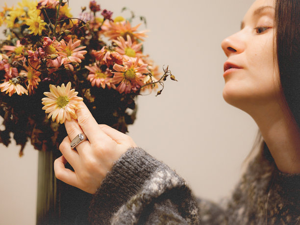 年轻女子享受秋日花香，将娇嫩的花朵凑近脸庞。温暖舒适的室内氛围，非常适合健康、正念、生活方式和美容主题的素材。图片下载