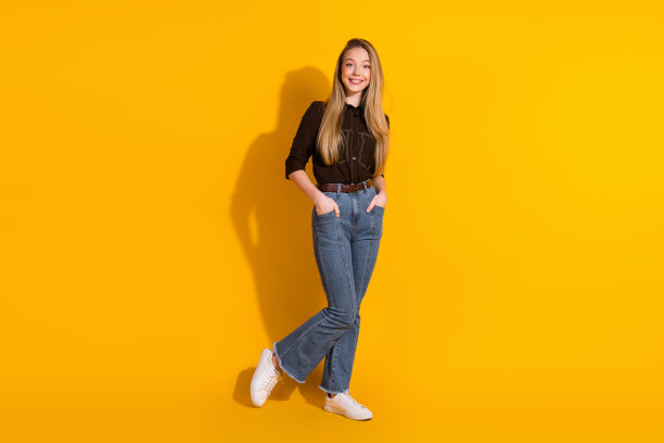 年轻女子穿着休闲时尚，在明亮的黄色背景前摆姿势，用于生活方式素材图片图片下载