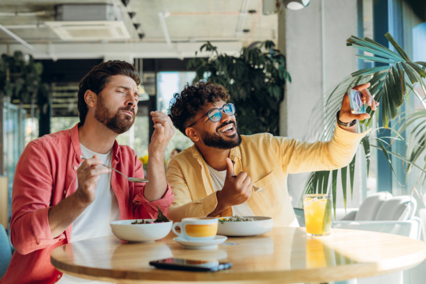 两位英俊快乐的多元化朋友坐在咖啡馆，品尝美味食物，并拍摄照片和视频图片下载