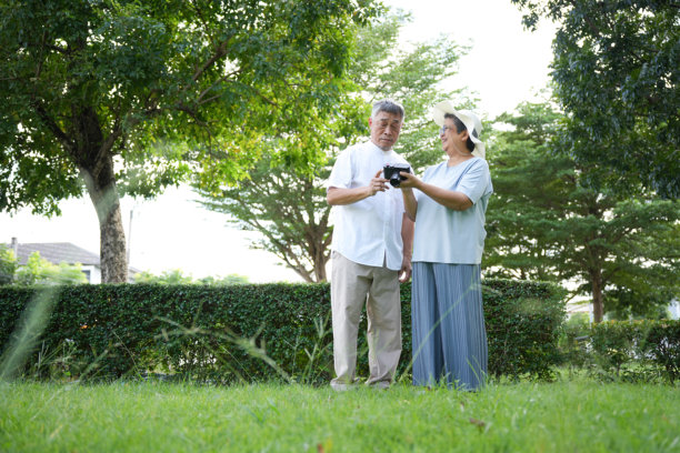 老年夫妇在户外用相机查看照片，一对老人在公园里一起学习摄影，一对老人在公园里探索摄影图片下载