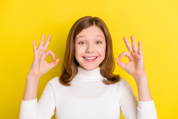 一个年轻快乐的女孩，带着积极的微笑，竖起大拇指表示“好”或“酷”，在黄色背景上展示完美，表情独立。图片下载