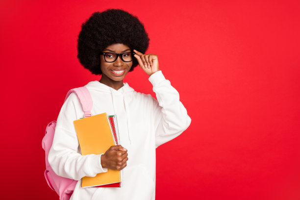 照片：一位留着可爱卷发、手持书籍、身背书包、戴着眼镜、穿着白色运动服的年轻女士，背景是纯红色。图片下载