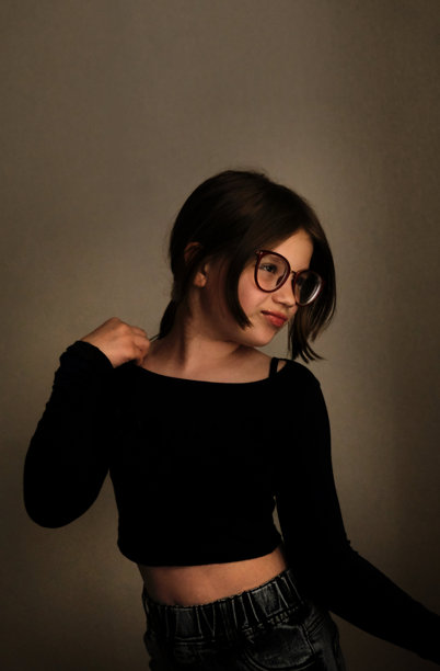 时尚模特。一位身穿黑色长袖露脐上衣和牛仔裤、戴着时尚眼镜的美丽年轻女孩的照片。低调肖像。望向别处图片下载