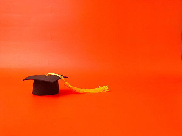 图片展示了毕业帽（也称为学士帽或方帽）在橙色背景上图片下载