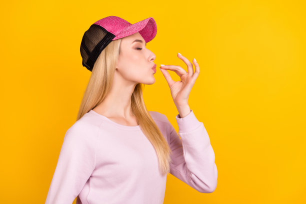 年轻漂亮女孩的侧面头像，在黄色背景上做出美味的手势图片下载