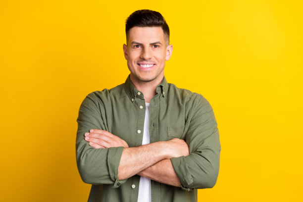 照片肖像，一个男人微笑着，双手交叉，背景是鲜艳的黄色图片下载