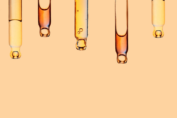 浅橙色背景下的五支装有面部精华的玻璃滴管。正面特写镜头，展示液体凝胶或精油，作为抗衰老化妆品广告的横幅。图片下载