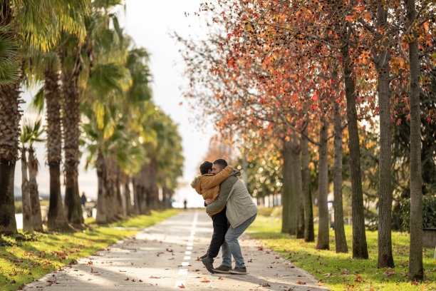 一个孩子跑进城市公园，跳到父亲的腿上，拥抱了他。系列照片的一部分图片下载