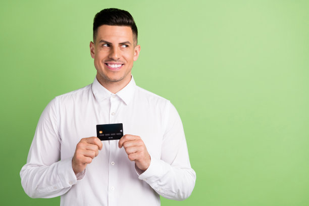 照片：一位穿着白色衬衫、面带微笑、手持银行卡、眼神望向远方的迷人绅士，背景为孤立的绿色图片下载