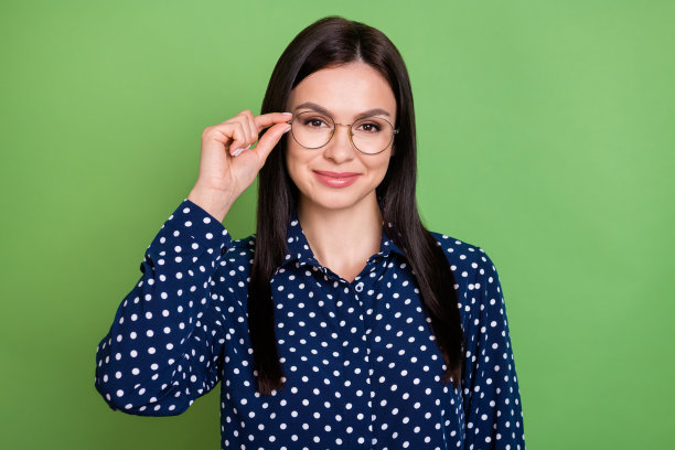 照片：一位漂亮的、吸引人的年轻女子戴着眼镜，手指放在脸部，背景为闪亮的绿色。图片下载