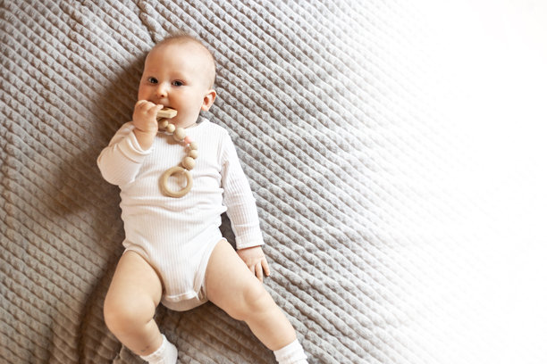 一个孩子趴在有纹理的毯子上，玩着一个木制的环保玩具。这张图片捕捉了一个充满童趣的瞬间，强调了可持续性和简约性，并留有充足的文字空间。图片下载