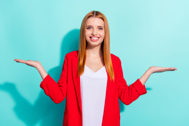 身穿红色西装外套、笑容甜美、露出双臂、背景为青色、留有空白空间的漂亮迷人橙发女士照片图片下载