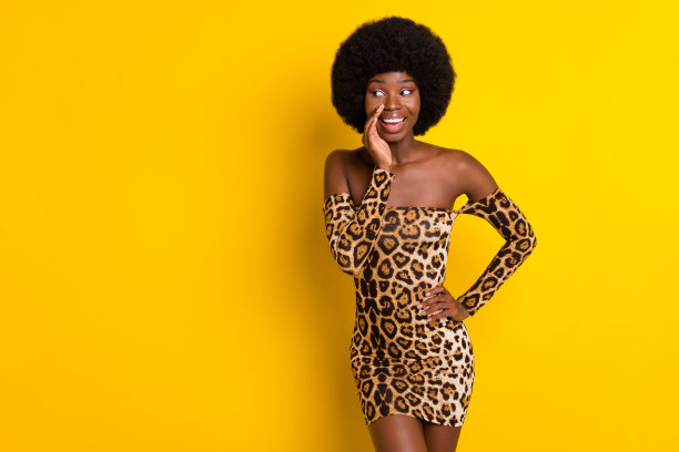 身穿豹纹服装的可爱有趣的深肤色女性，在孤立的黄色背景前对着虚空低语的特写照片图片下载