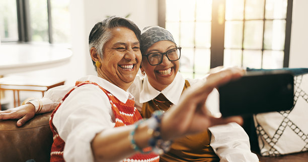 沙发上，快乐的年长女性们周末在家中合影留念，享受着亲情。客厅里，年长女性们带着友谊的笑容，连接彼此，拍摄照片。图片下载