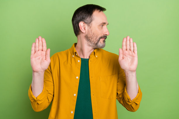 照片：迷人的、表情严肃的绅士穿着橙色衬衫，伸出双手，望向虚空，背景是绿色的。图片下载