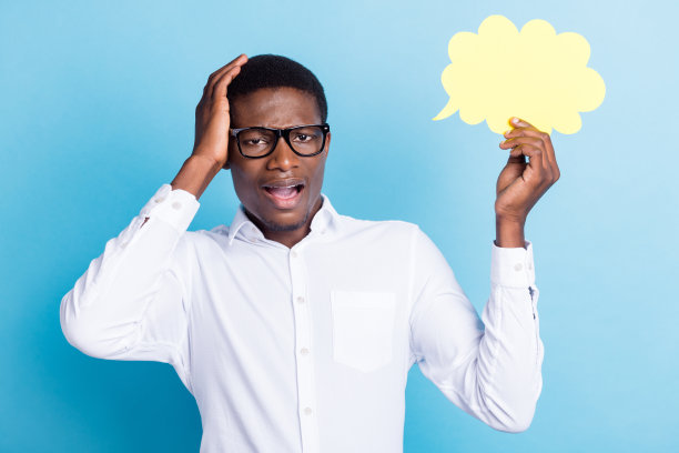 照片：穿着白衬衫的甜美、惊讶的深肤色男子，一只手托着头，另一只手拿着一个思维云，置于孤立的蓝色背景的空白空间中。图片下载