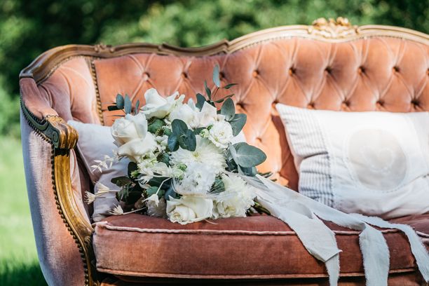 新娘捧花，由白玫瑰和绿叶优雅地 arranged 在复古沙发上。图片下载