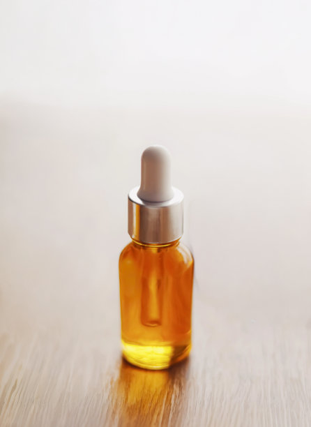 带有滴管的护肤品包装，装有金黄色液体精华或精油，置于木质表面上图片下载