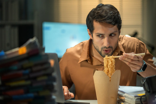 拉丁美洲商人加班，在办公桌前吃泡面。图片下载