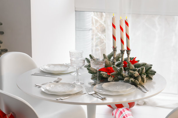 节日圣诞餐桌布置，有结霜的松枝、蜡烛和白色盘子，摆放在圆桌上。图片下载