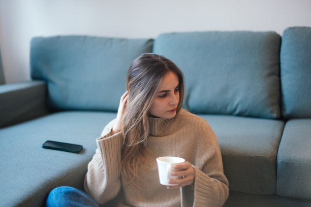 一位女子坐在沙发上，品尝着茶，旁边放着手机——素材照片图片下载