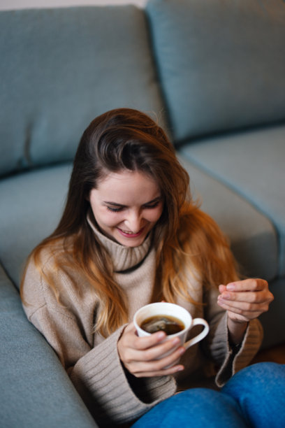身穿舒适毛衣的女子在沙发上喝茶 - 库存照片图片下载