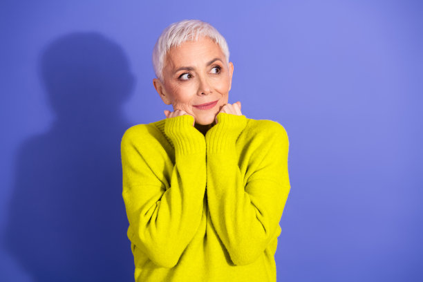 一位穿着亮黄色毛衣的成熟的女士，在紫罗兰色背景前，展现出喜悦、休闲时尚和生活方式品牌形象。图片下载