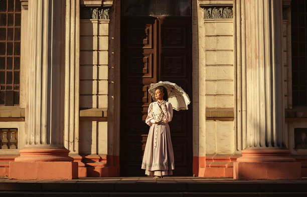 一位优雅的女士身着复古连衣裙，在温暖的阳光下撑着蕾丝阳伞。图片下载