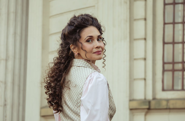 一位优雅的女士身着复古连衣裙，站在古老的石柱旁图片下载