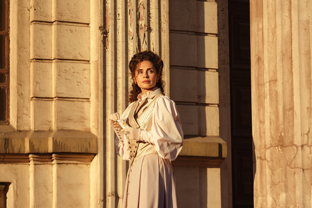 身着复古裙装的女子在古老大教堂的柱子旁，将一封信贴近心口。图片下载