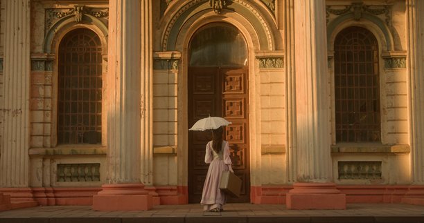 一位身着复古连衣裙的女士，手持雨伞和行李箱，站在一座古老大教堂的门前。图片下载
