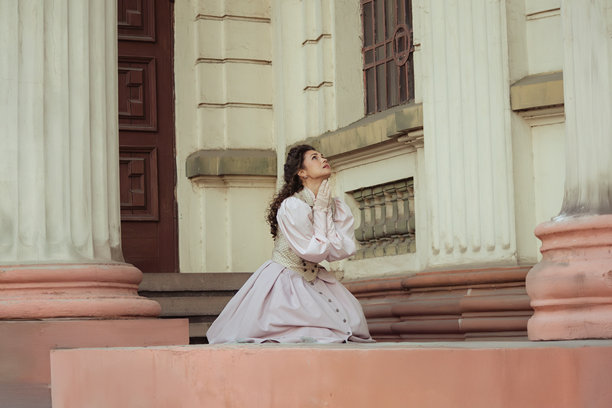 一位身穿复古连衣裙的优雅女士站在古老的石柱旁图片下载