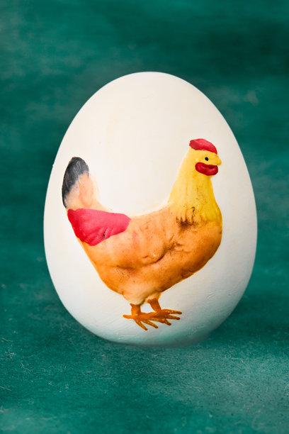 一个带有鲜艳手绘鸡形图案的白鸡蛋，在纹理感十足的蓝绿色背景下格外醒目。非常适合复活节、农场或手工主题。图片下载