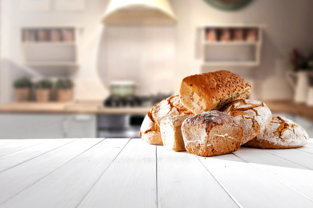 温暖诱人的照片，展示了摆放在白色木桌上的各种面包，背景是舒适的厨房，非常适合美食博客图片下载