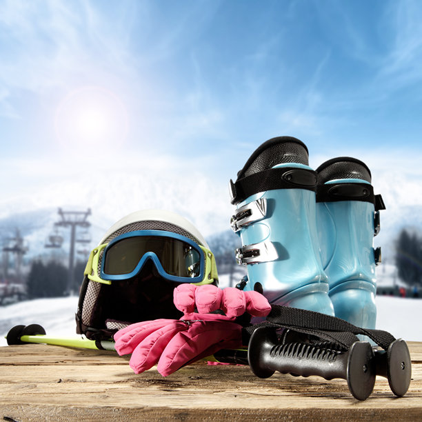 冬季运动装备照片，展示了放在木桌上的滑雪靴、头盔、手套和雪杖，背景是雪山景观图片下载