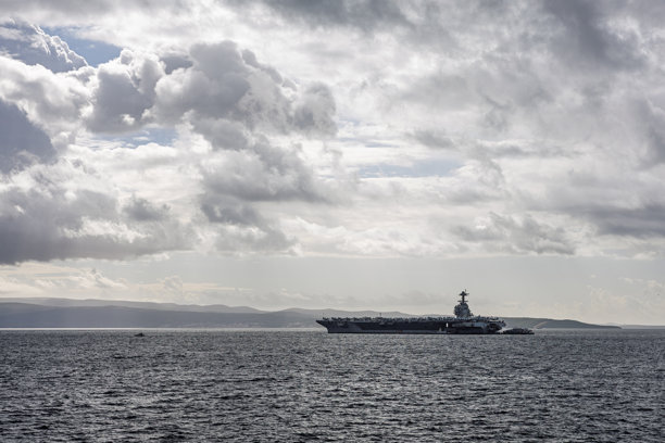 厚重的航空母舰在阴云密布的天空下，剪影般映衬在平静的海面上，适用于军事和海事素材图片下载