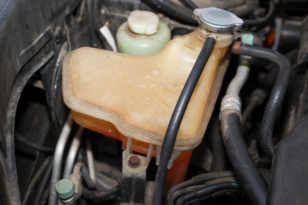 特写镜头展示了汽车冷却系统中的膨胀水箱，里面装着橙色液体，强调了发动机维护的重要性。图片下载