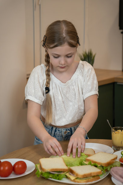 女孩在厨房里小心翼翼地往面包上铺食材，制作新鲜的三明治作为午餐，注重健康饮食并培养烹饪技能。竖直照片图片下载