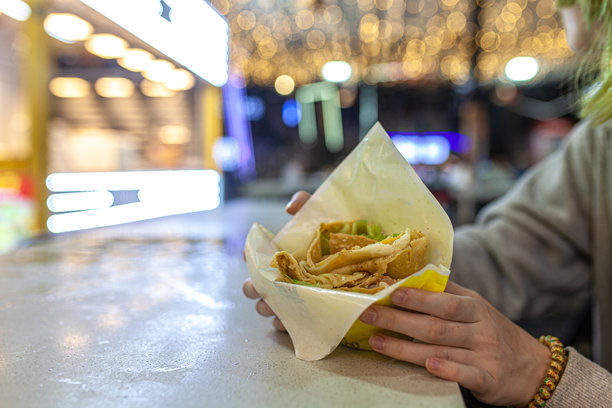 在中国海南岛三亚的夜市上，女孩的手拿着包着虾、生菜和酱料的折叠咸味鸡蛋煎饼卷，外面用纸包好。图片下载