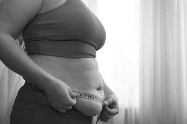 女孩在家用卷尺测量腰围。黑白照片图片下载