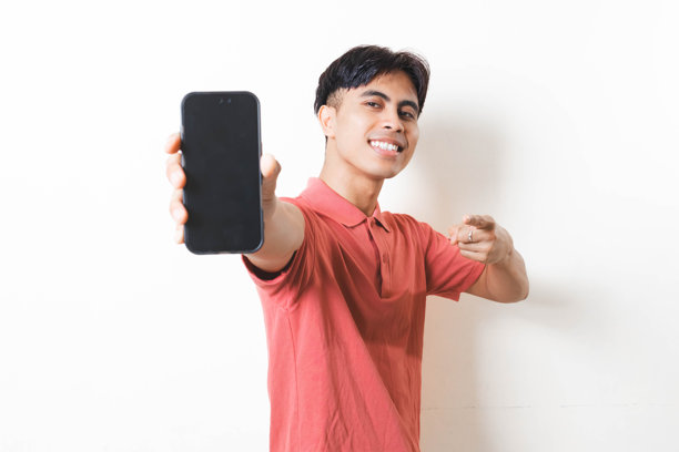 一个年轻男子指向空白的智能手机屏幕，用于应用程序或产品推广，非常适合在干净的白色背景上进行广告、在线服务和移动应用程序宣传。图片下载