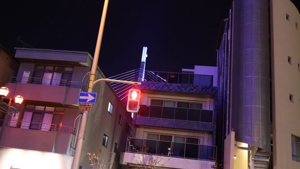 这张照片展示了夜晚的街景，背景中有一座醒目的建筑，其顶层窗户散发出蓝色的光芒。图片下载