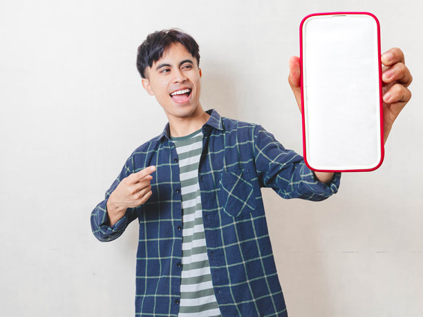 一位快乐的亚洲男子在白色孤立的背景上指向空白的智能手机屏幕，非常适合移动应用推广、广告和数字营销概念。图片下载