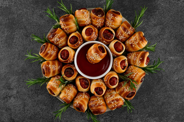 圣诞节烤肠圈搭配番茄酱，饰以新鲜迷迭香和芝麻。石板背景上的圣诞开胃菜。俯视角度，留有复制空间。图片下载