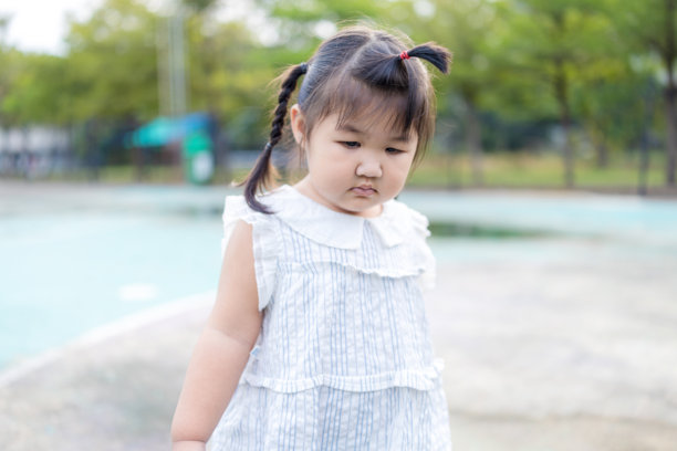 一个穿着白色连衣裙的可爱亚洲小女孩站在户外的游乐场上，白裙小女孩在克罗地亚盛开的公园背景前快乐微笑的肖像。高质量照片。图片下载